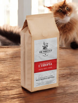 Ethiopia whole bean coffee bag from The Pawfect Brew on a wooden table with a cat in the background.