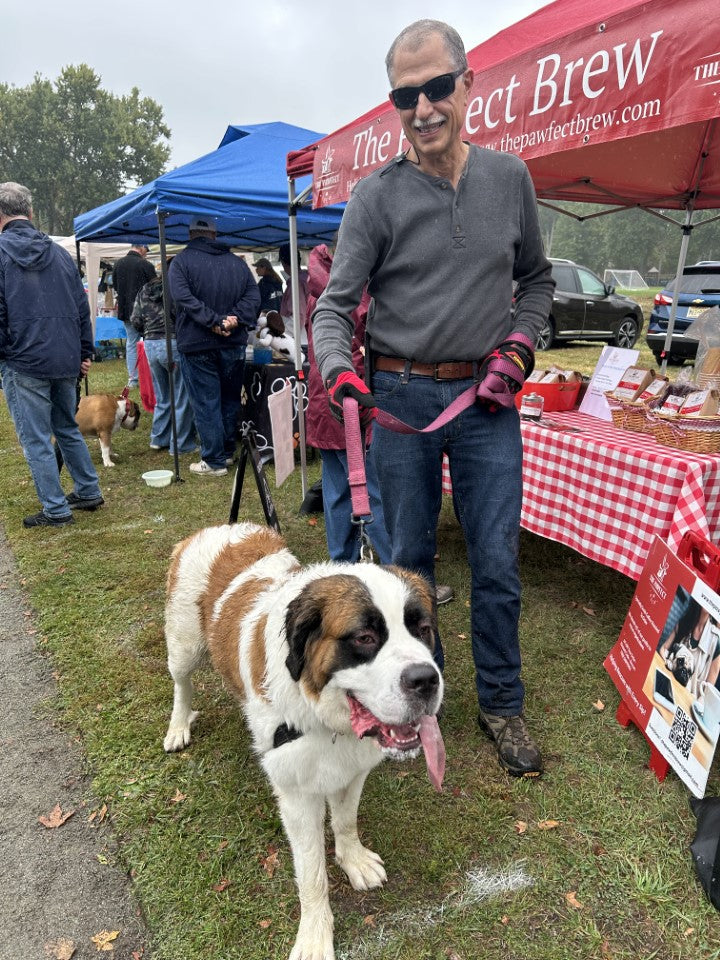 Man with a large dog at an outdoor event with booths and people in the background